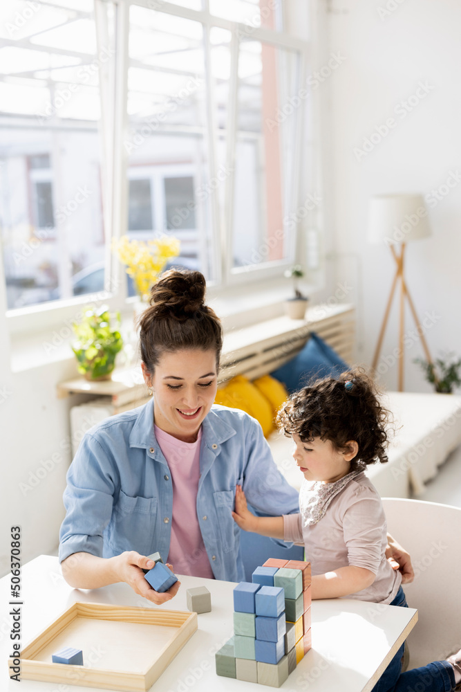 Mother sitting at table playing with daughter with building bricks Mother sitting at table playing with daughter with building bricks
