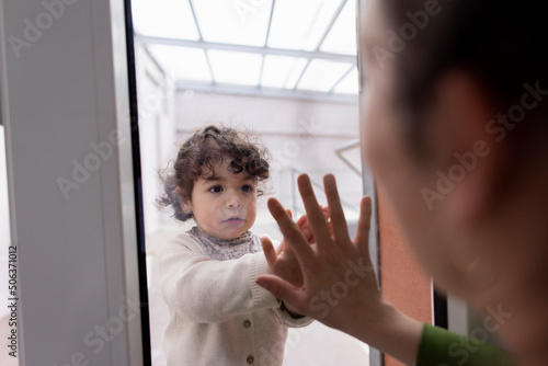 Mother and daughter touching hands separated through window pane