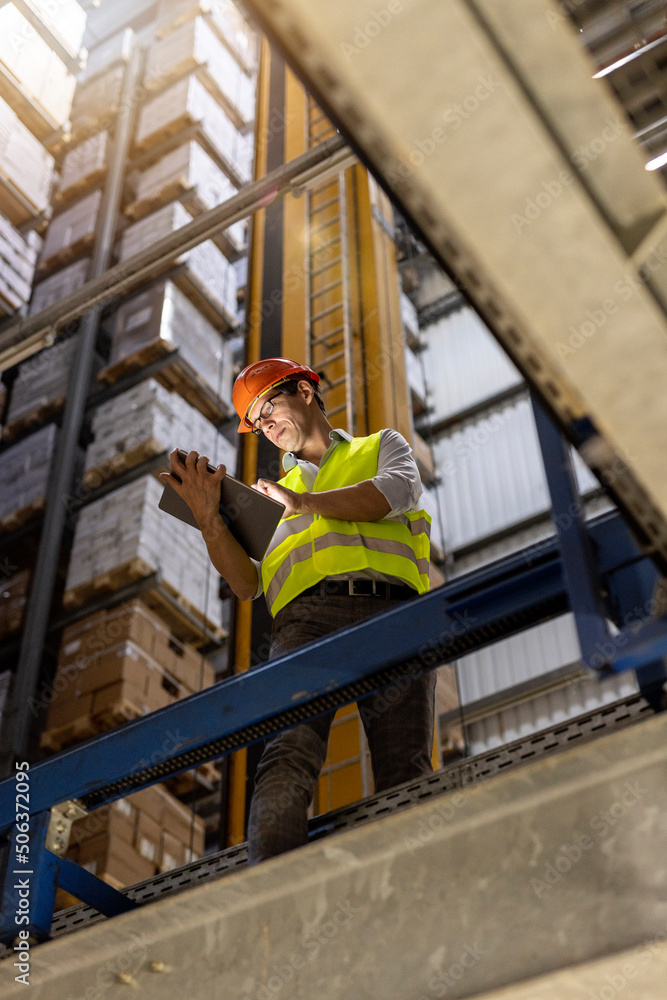 Worker checking list on tablet PC standing by railing in warehouse Worker checking list on tablet PC standing by railing in warehouse