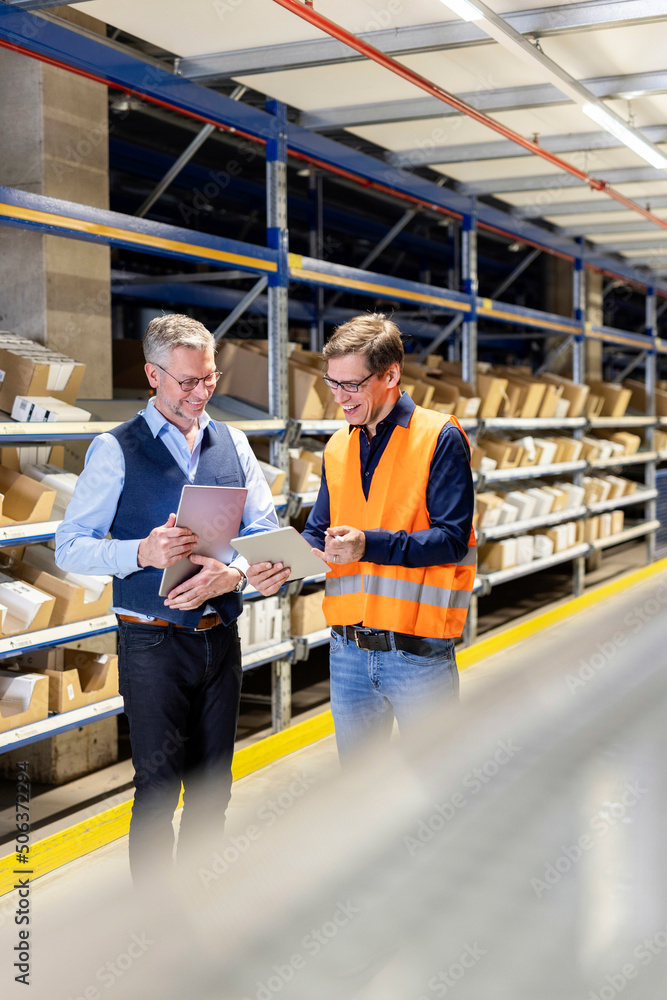 Happy worker and manager discussing over tablet PC in warehouse Happy worker and manager discussing over tablet PC in warehouse