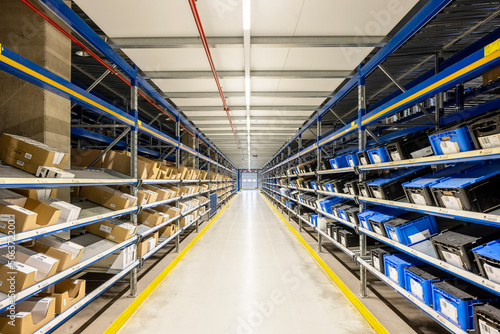 Empty straight aisle amidst cardboard boxes arranged on racks of warehouse photo