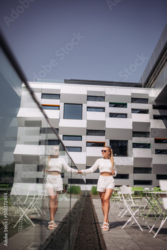 Portrait of young modern businesswoman model. Hot beautiful woman in a white suit posing against the backdrop of the street. Fashionable woman walking outdoors in sunglasses