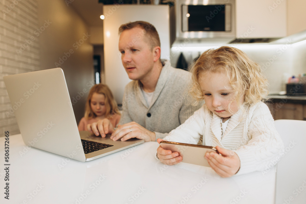 Daughter using smart phone by father working on laptop at home Daughter using smart phone by father working on laptop at home