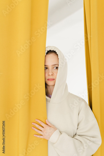 Woman peeking through yellow curtain at home