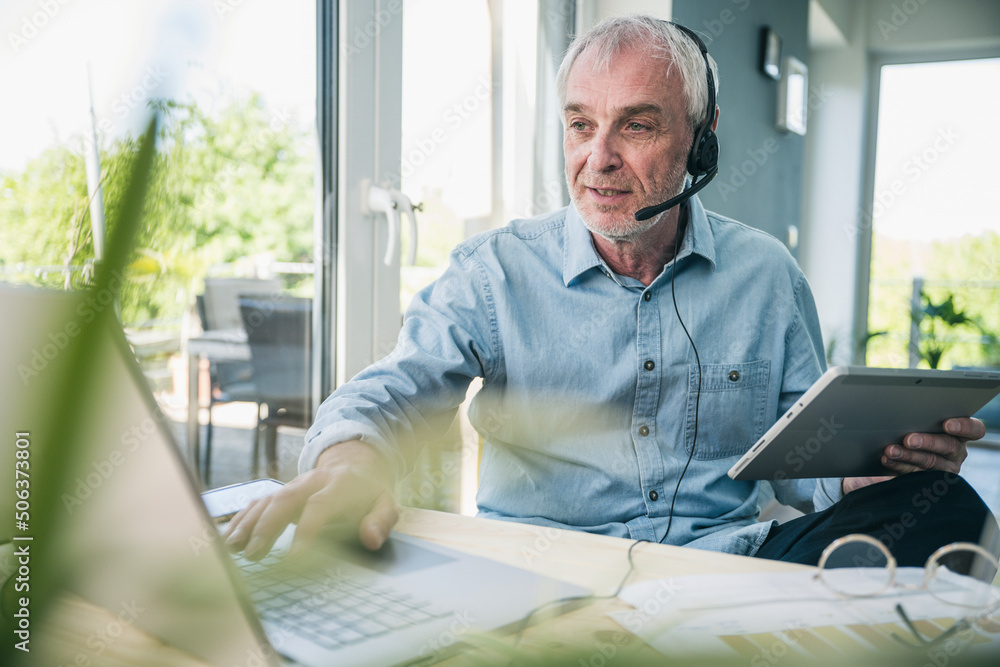 Senior businessman wearing headset working on laptop at home Senior businessman wearing headset working on laptop at home