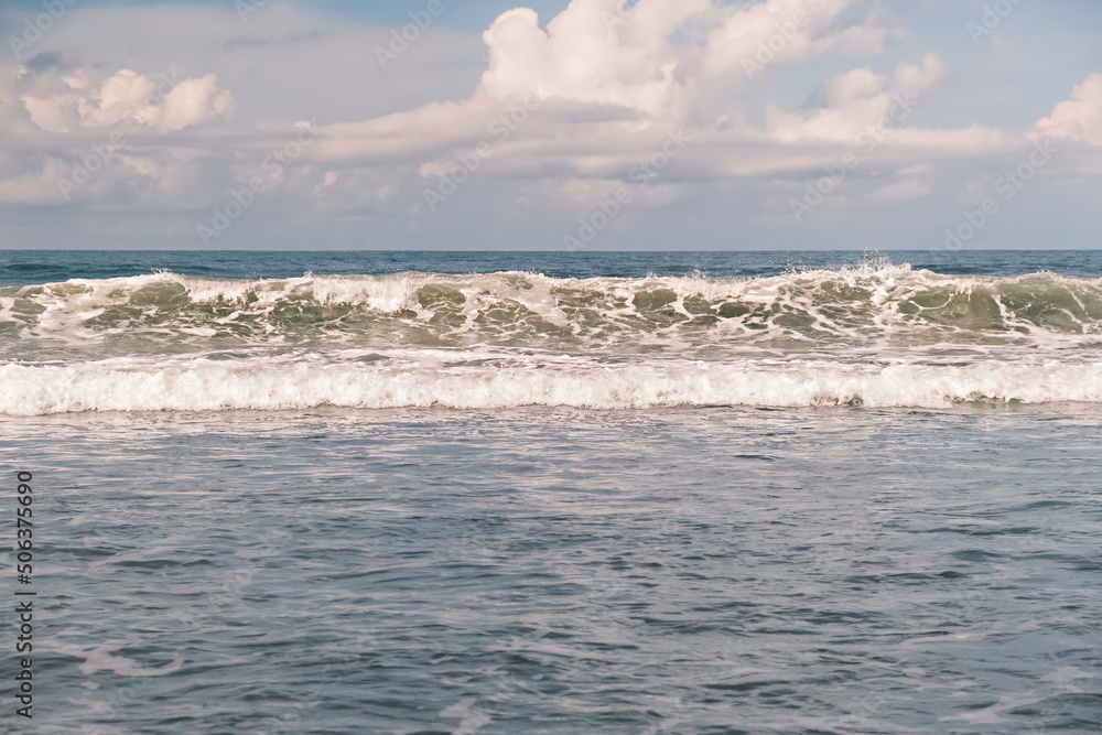 Ocean waves. Big surfing waves breaking onto beach at Bali, Indonesia. Scenic view of high emerald waves with white foam moving towards the shore on a tropical island in Indonesia.