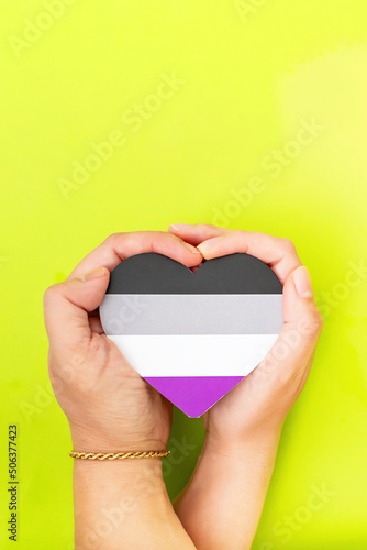 Woman hands hold heart in the colors of asexual flag on green background. LGBT concept, Pride month. Top view, copy space.