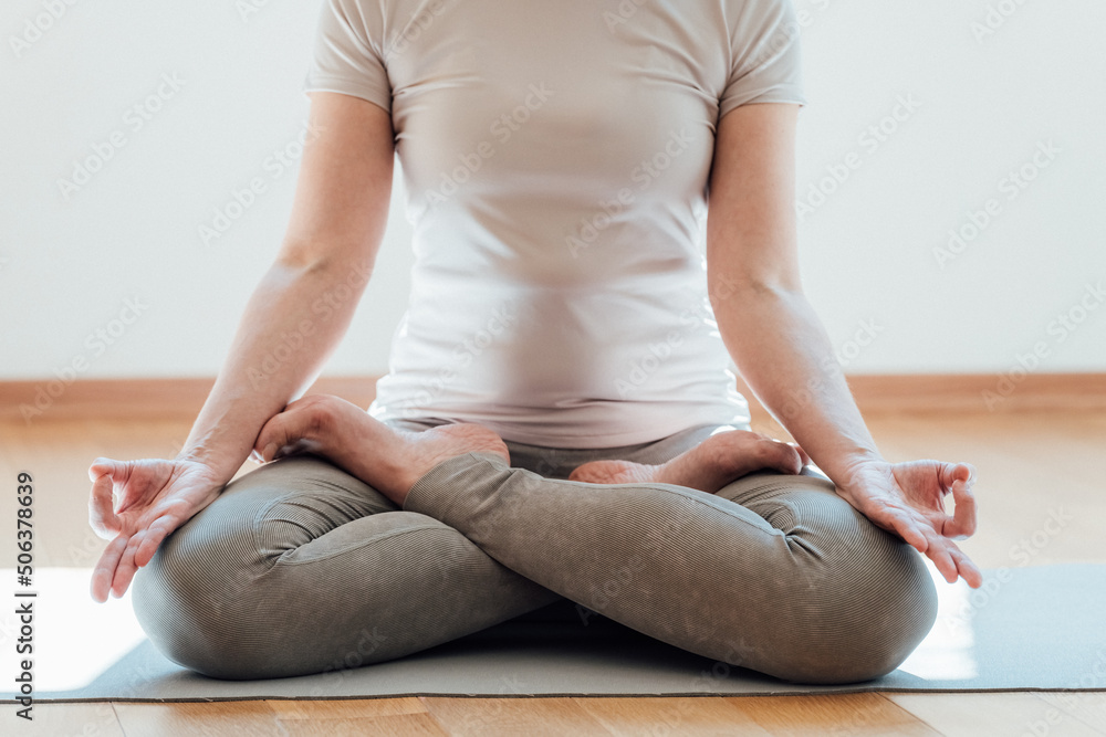 Cropped view of the senior woman in casual clothes meditating and sitting on lotus pose at home. Sport and recreation concept