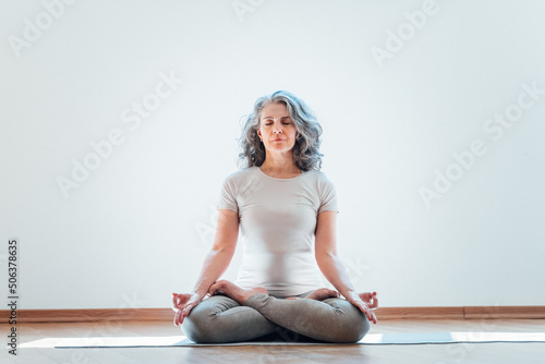 Full length view of the elderly woman practicing yoga at lotus pose in studio. Mature yoga teacher is take time for herself at home