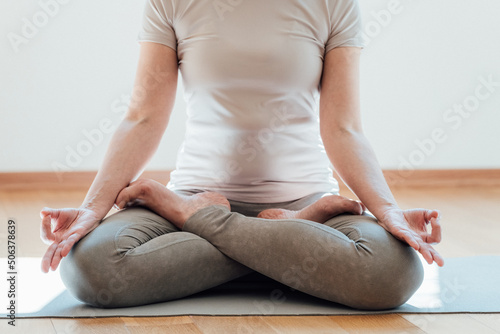Fototapeta Naklejka Na Ścianę i Meble -  Cropped view of the senior woman in casual clothes meditating and sitting on lotus pose at home. Sport and recreation concept