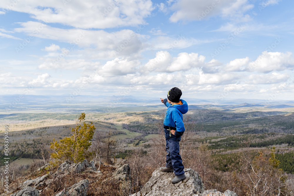 child standing high on a stone pointing a finger forward at the mountain, hiking in the forest, children's hiking trail, extreme young climber, family vacation