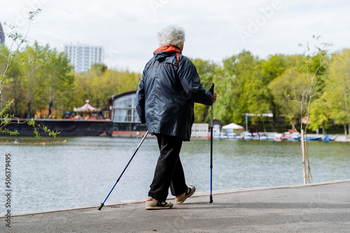 A woman trains to walk with poles, active sports for pensioners, Nordic walking in the park, a summer walk in the fresh air, a grandmother walks along the path.