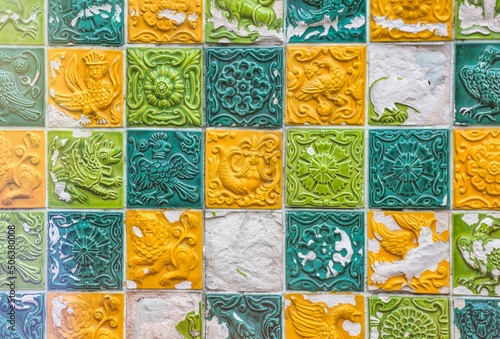 Decorative textured clay tile background on the wall with various ancient drawings of different colors. A wall with ancient ceramic tiles of different colors. Beautiful multicolored background.