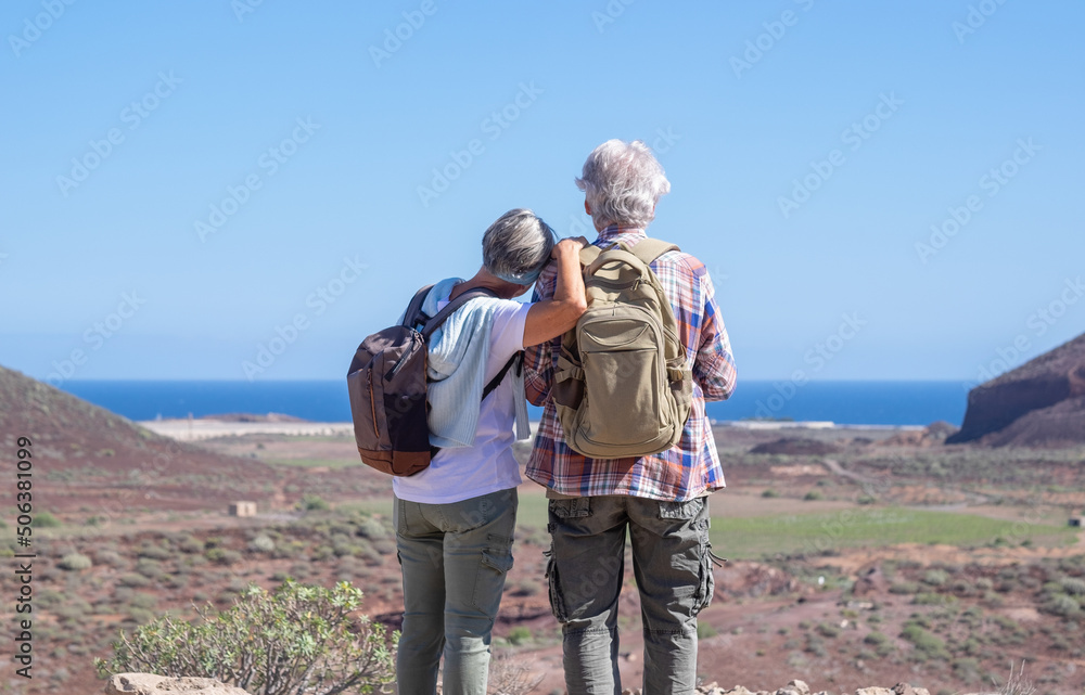 Rear view of elderly caucasian couple in outdoors activity on hill looking horizon. Landscape and sea in background