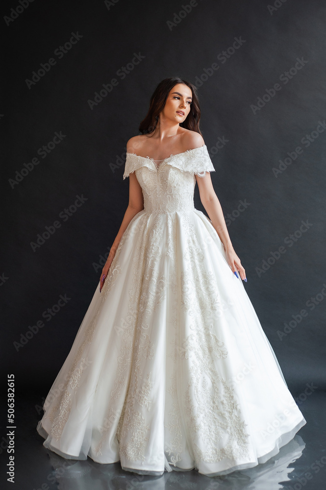 Beautiful young sexy model female bride with dark hair in gorgeous glossy long light wedding dress posing in dark studio Beautiful young sexy model female bride with dark hair in gorgeous glossy long light wedding dress posing in dark studio