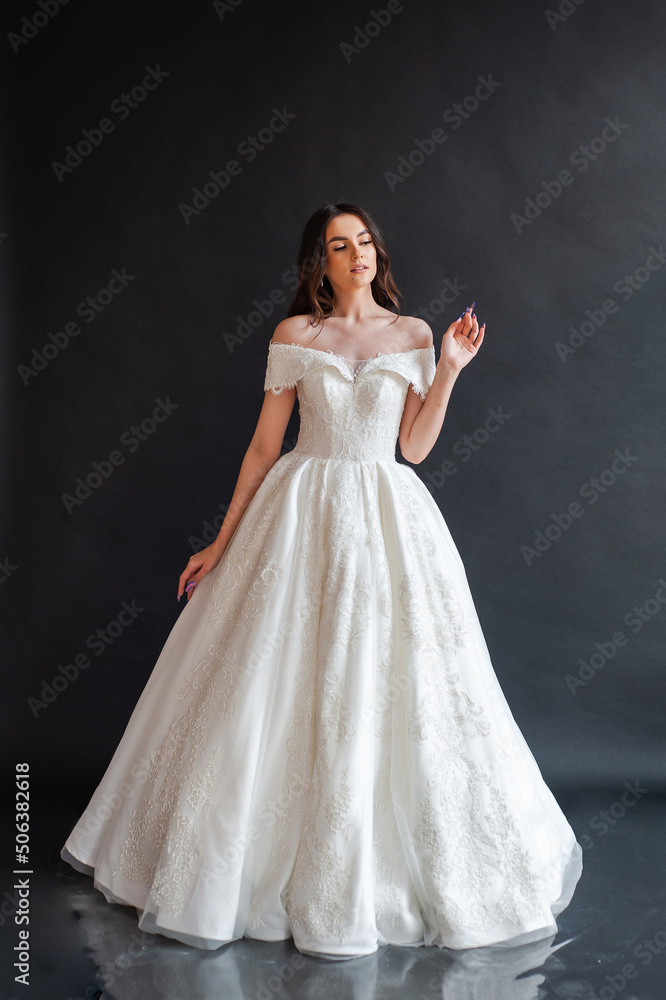 Beautiful young sexy model female bride with dark hair in gorgeous glossy long light wedding dress posing in dark studio Beautiful young sexy model female bride with dark hair in gorgeous glossy long light wedding dress posing in dark studio