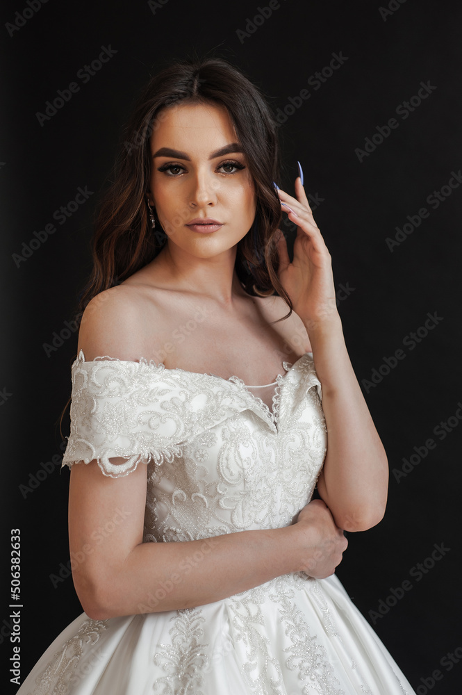 Beautiful young sexy model female bride with dark hair in gorgeous glossy long light wedding dress posing in dark studio Beautiful young sexy model female bride with dark hair in gorgeous glossy long light wedding dress posing in dark studio