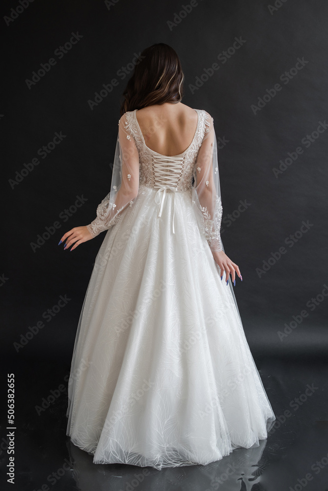 Beautiful young sexy model female bride with dark hair in gorgeous glossy long light wedding dress posing in dark studio Beautiful young sexy model female bride with dark hair in gorgeous glossy long light wedding dress posing in dark studio