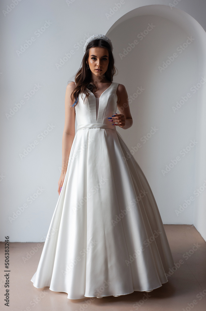Fototapeta premium Charming young bride in luxurious wedding dress. Pretty girl in white. Emotions of happiness, laughter and smile, gray background