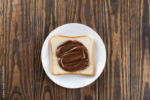 A slice of toast bread with chocolate hazelnut paste in a plate on a wooden table. Horizontal orientation, top view.