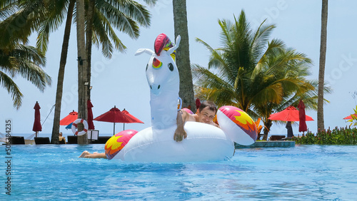 Happy funny man successfully jump onto floating inflatable unicorn in swimming pool in tropical hotel to ride. Crazy male tourist have fun on giant toy in water. Summer vacation, holiday concept. © TravelMedia