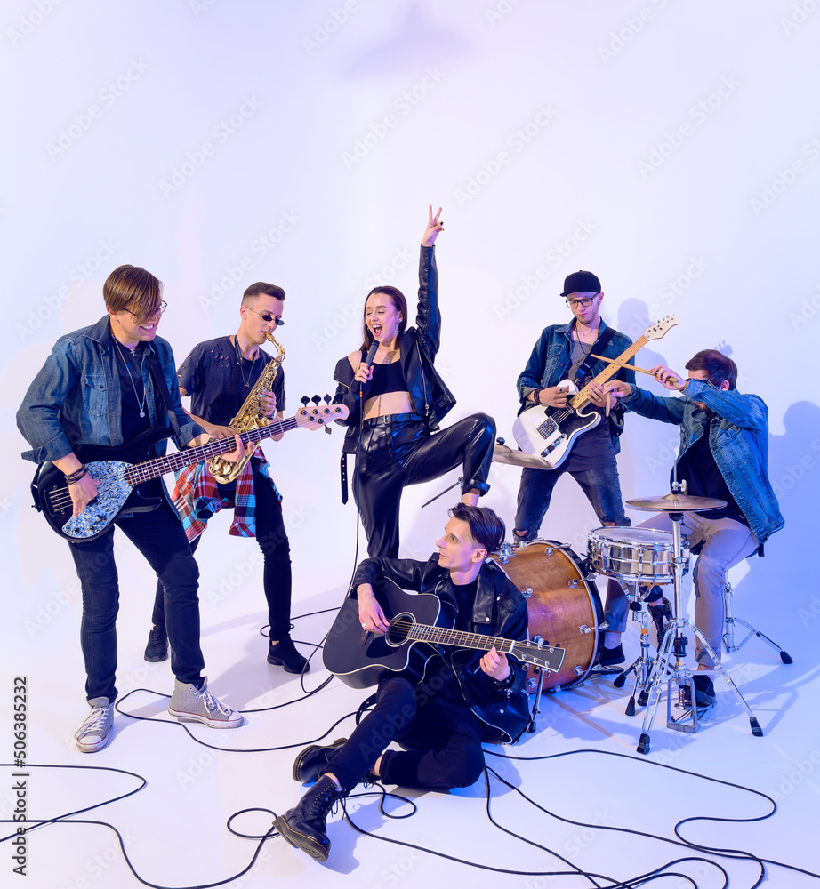 Fototapeta premium Young rock band of six people emotionally playing and singing on a white background with blue light around