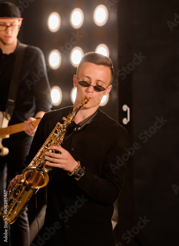 Young saxophone playing the saxophone on a loft interior background with light bulbs