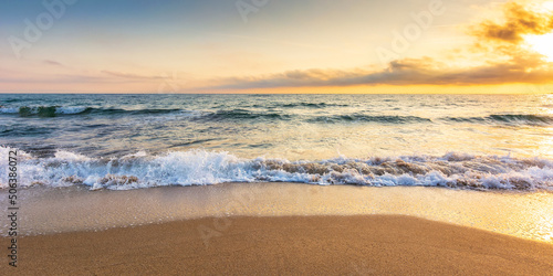 sandy beach at sunrise. beautiful seascape background. calm waves washing the shore. clouds glowing in morning light. summer vacation and relaxing recreation concept