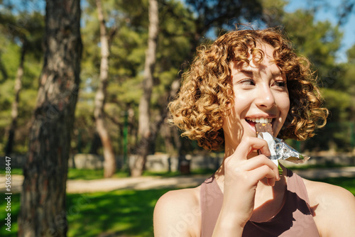 Athletic woman eating a protein bar. Fitness beautiful woman eating a energy snack outdoor. Copy space. Healthy food, outdoor sports concepts.