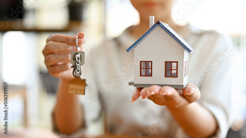 Female real estate agent or property broker holding a house model and a house keys.