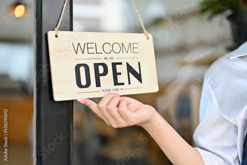 Female barista holding a coffee shop welcome sign in front of the coffee shop.