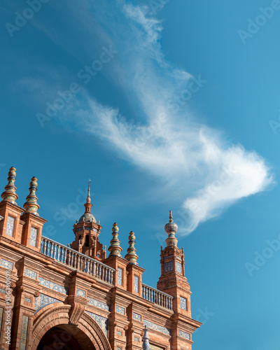 Small part of the facade of the Plaza de España in Seville with soft clouds in a blue sky.