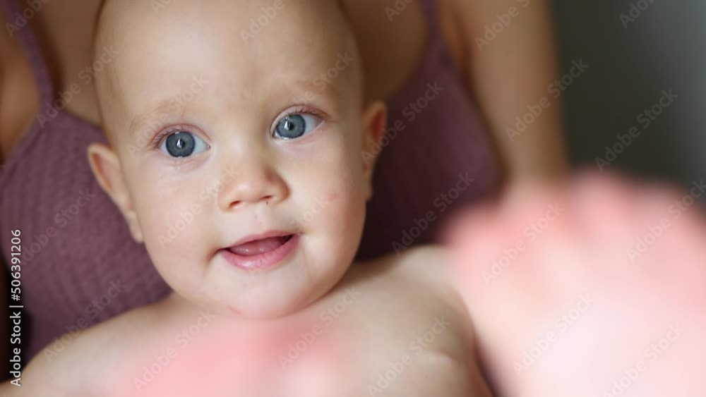portrait of funny blue eyes baby infant sitting on mother knees playing feet, smiling, looking to camera. toddler child kid naked, opening mouth with white teeth. happy childhood family concept portrait of funny blue eyes baby infant sitting on mother knees playing feet, smiling, looking to camera. toddler child kid naked, opening mouth with white teeth. happy childhood family concept