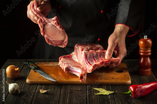 The chef is holding a piece of raw meat with a bone in the kitchen. Slicing pork ribs by the hands of a butcher. European cuisine