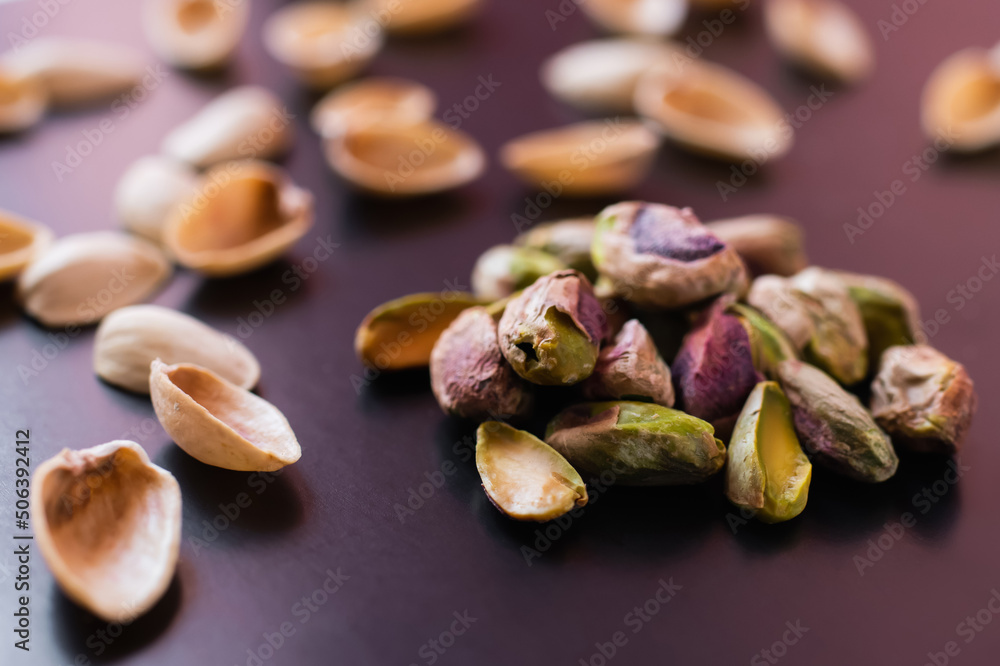 close up of nutshells and salty green pistachios on black
