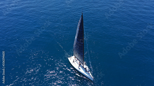 Aerial drone birds eye view photo of beautiful sailboat with blue sails cruising in the deep blue Aegean sea, Greece © aerial-drone