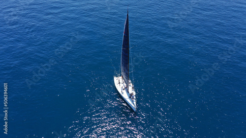 Aerial drone birds eye view photo of beautiful sailboat with blue sails cruising in the deep blue Aegean sea, Greece