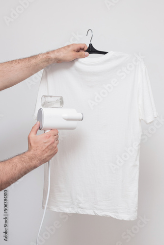 Iron the T-shirt with a manual steamer on a gray background. close-up
