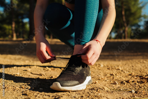 Runner woman wearing blue yoga pants and black sneaker shoes standing on city park, outdoors tying lace running shoes getting ready for run. Jogging girl exercise motivation health and fitness.