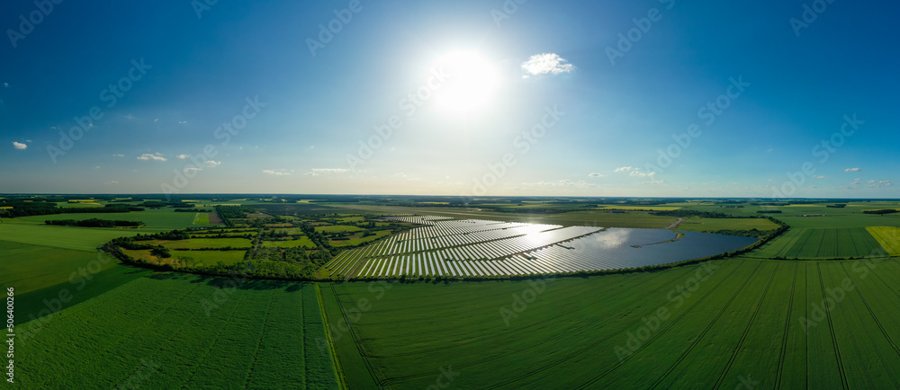 Panorama. Large solar power plant on a picturesque green field. Solar panels in aerial view. Power plant using renewable solar energy with sun. Alternative source of electricity.
