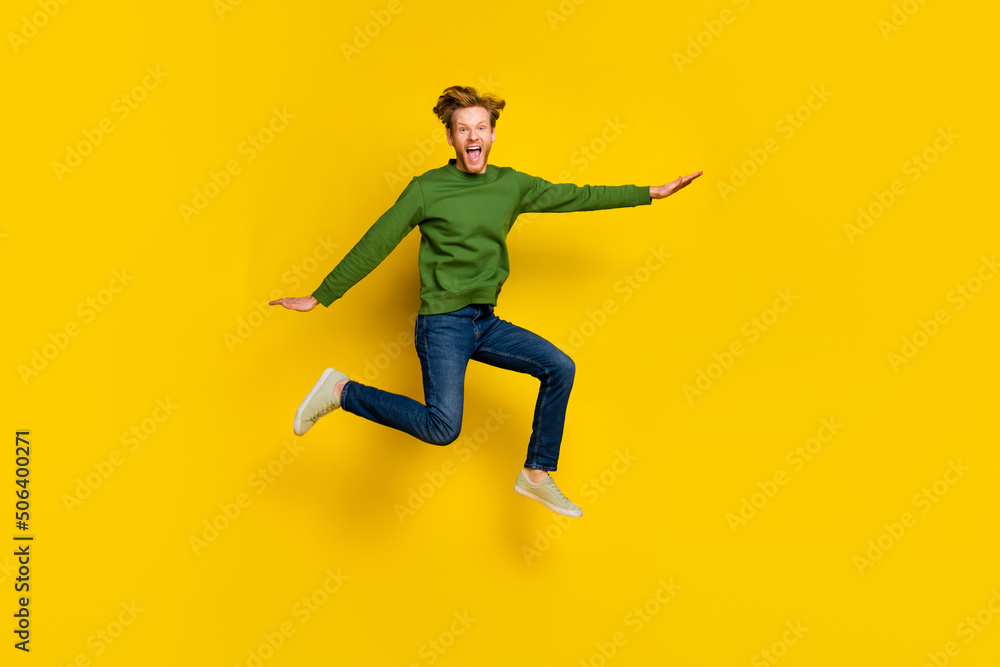 Full length photo of excited impressed man wear green pullover jumping high isolated yellow color background Full length photo of excited impressed man wear green pullover jumping high isolated yellow color background