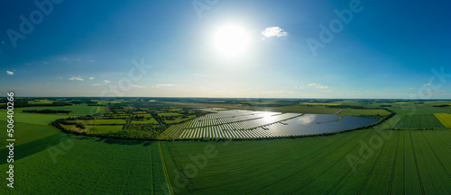 Obraz na płótnie Panorama. Large solar power plant on a picturesque green field. Solar panels in aerial view. Power plant using renewable solar energy with sun. Alternative source of electricity. w salonie
