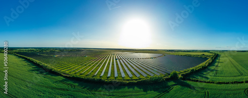 Panorama. Large solar power plant on a picturesque green field. Solar panels in aerial view. Power plant using renewable solar energy with sun.  Alternative source of electricity.