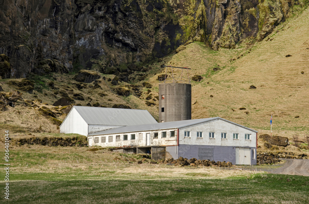 Skogar, Iceland, April 22, 2022: modern agricaultural barns and silo against the backdrop of a rocky cliff