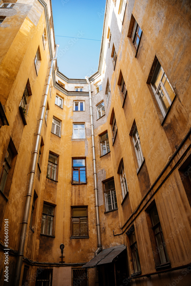 Saint Petersburg, Russia, 17 October 2021: Hight narrow courtyards called well in center, old architecture, Bottom up view, piece of sky is visible between profitable yellow houses, Dark inner