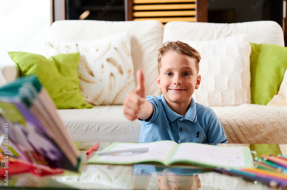 Caucasian school boy doing homework and shows thumb up gesture Caucasian school boy doing homework and shows thumb up gesture