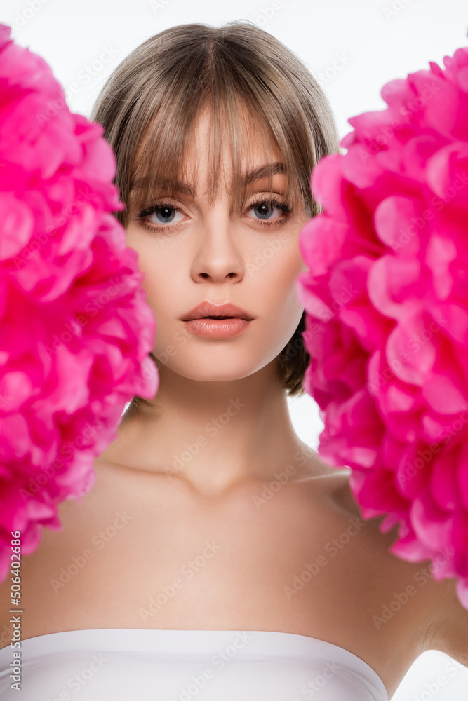 young woman with blue eyes looking at camera through blurred pink flowers isolated on white