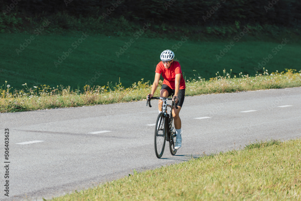 Obraz premium Caucasian girl cyclist with professional racing sports gear riding on an open road cycling route