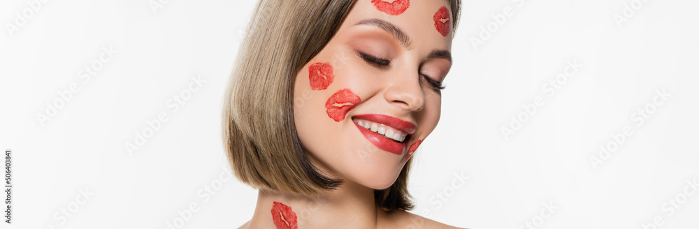 pleased young woman with red kiss prints on cheeks and body smiling isolated on white, banner pleased young woman with red kiss prints on cheeks and body smiling isolated on white, banner