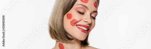pleased young woman with red kiss prints on cheeks and body smiling isolated on white, banner